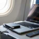 Batterie externe rechargeant un ordinateur portable posé sur une tablette d’avion pendant un voyage.
